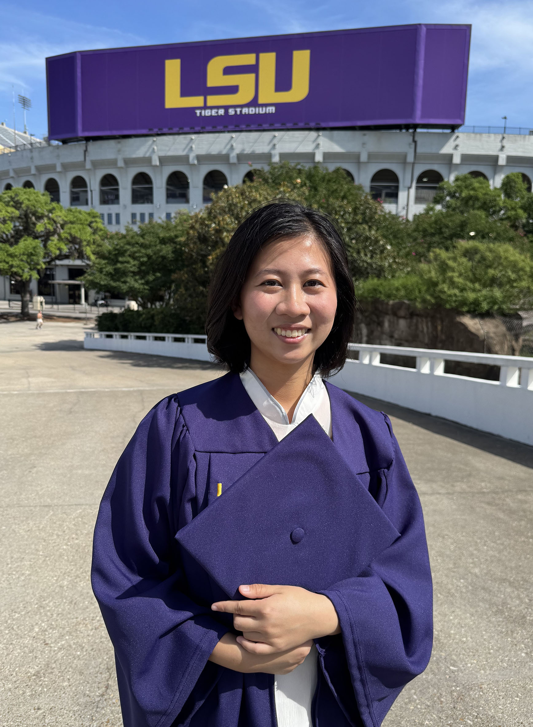 Emma Tsai in cap and gown in front of LSU Stadium