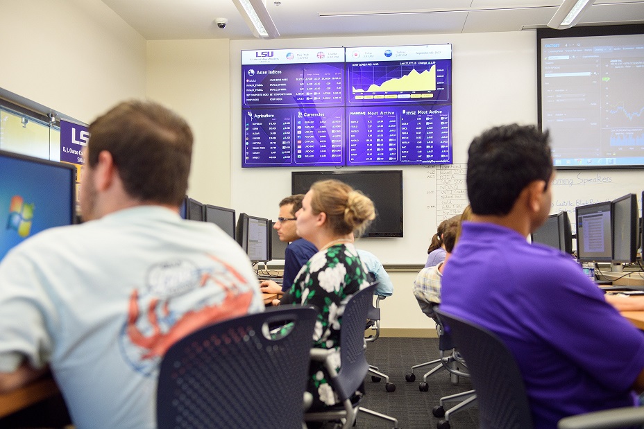 Students working on comptuers in SMART Lab while financial data is displayed in the background