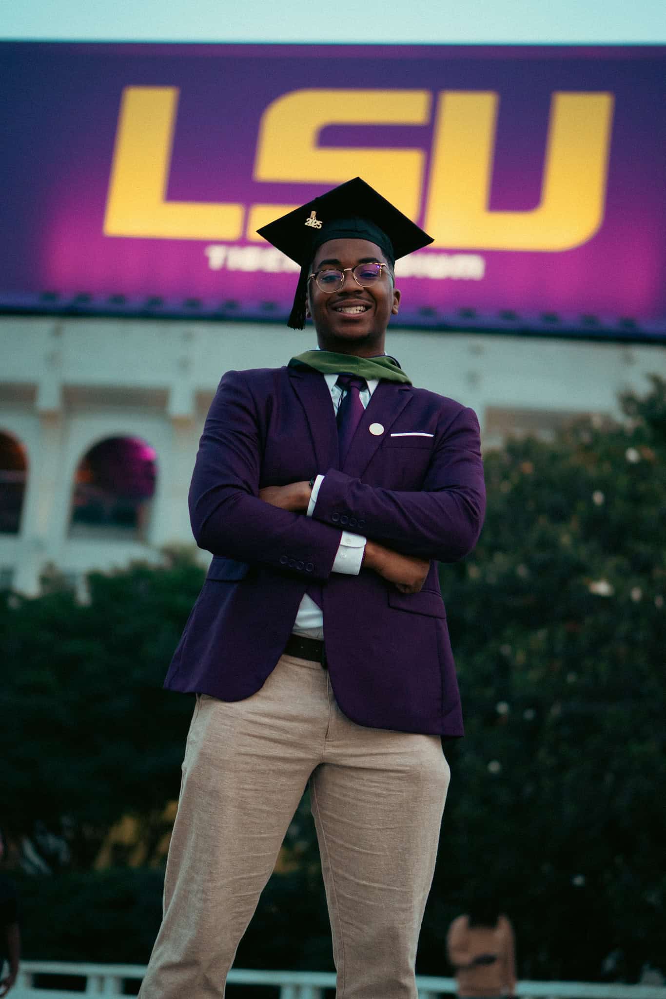 Jared Smith in graduation regalia standing in front of the LSU Tiger Stadium sign