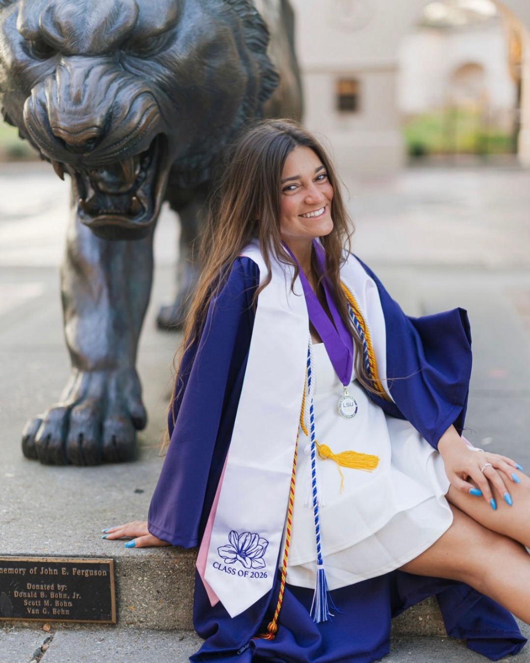 Gianna Vaccaro in her commencement regalia posing next to a bronze statue of Mike the Tiger