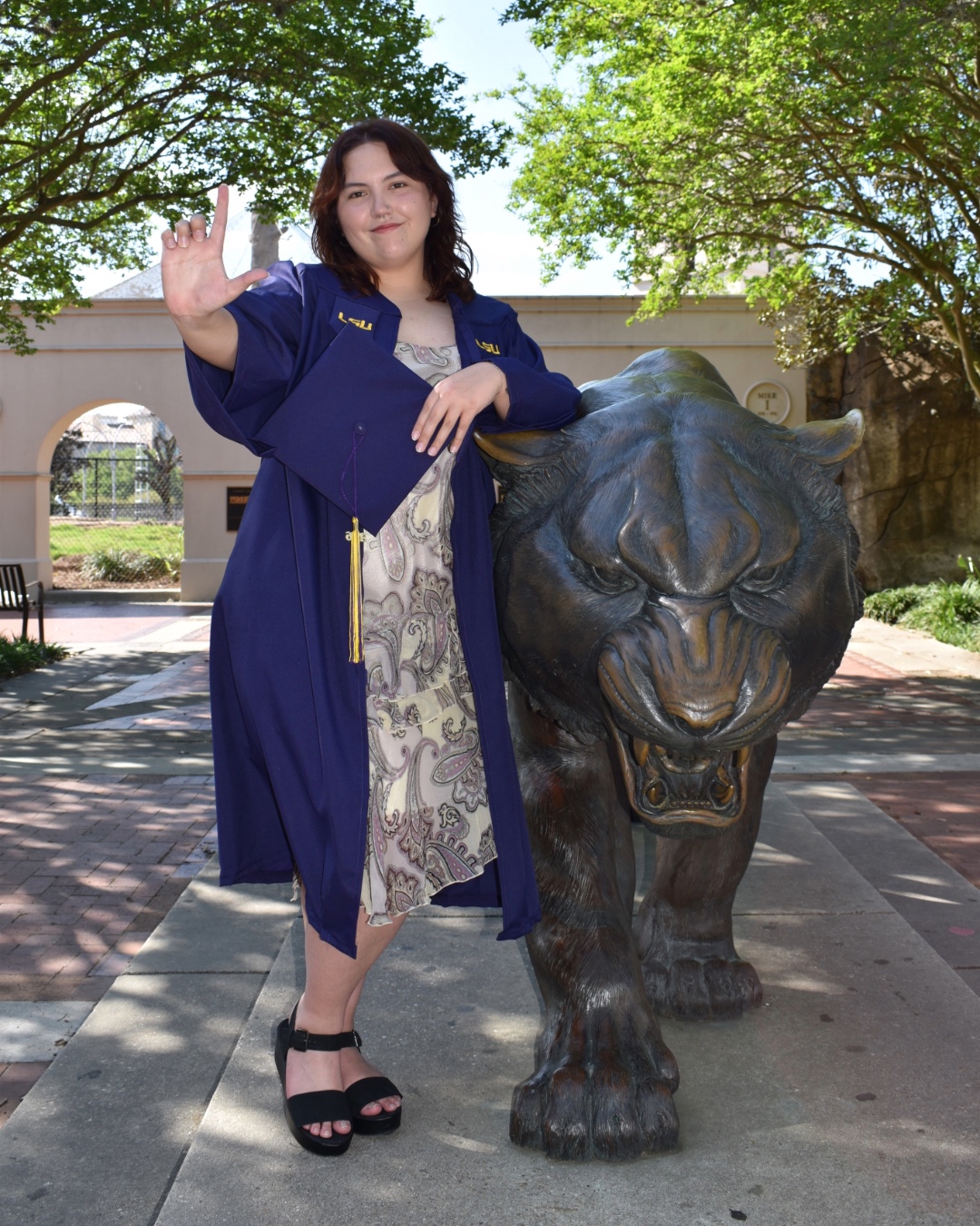 Jaden Frew posing with a bronze statue of Mike the Tiger in her commencement regalia