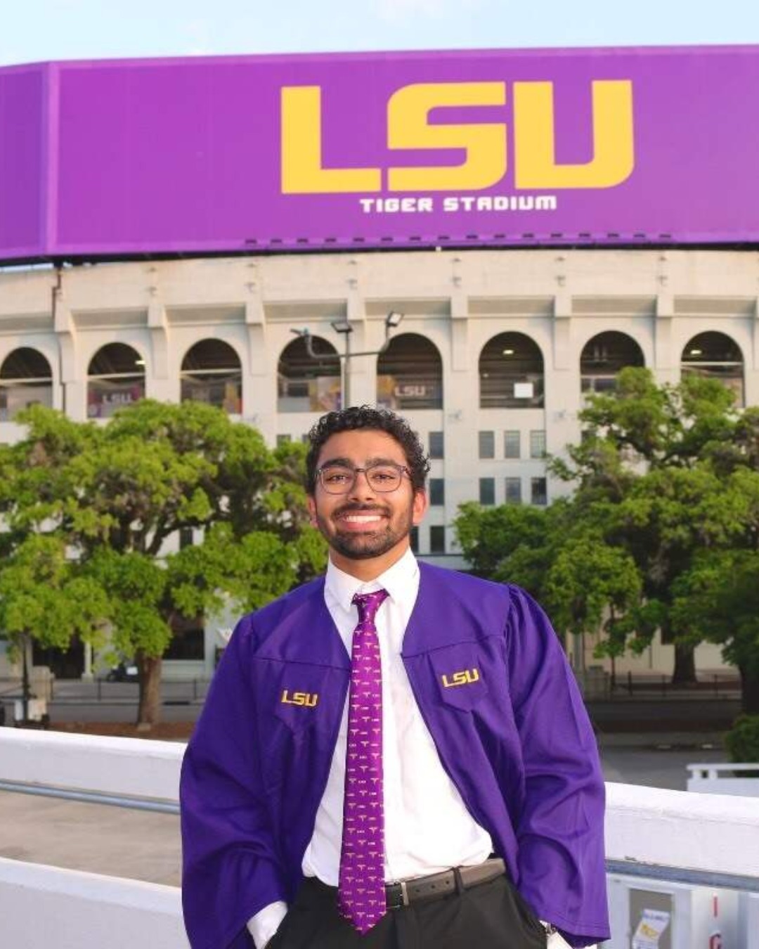Photo of LSU Honors student Mihir Babbar in his commencement regalia in front of Tiger Stadium